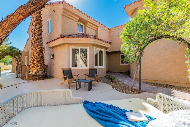 back of property with a tile roof, a patio area, and stucco siding