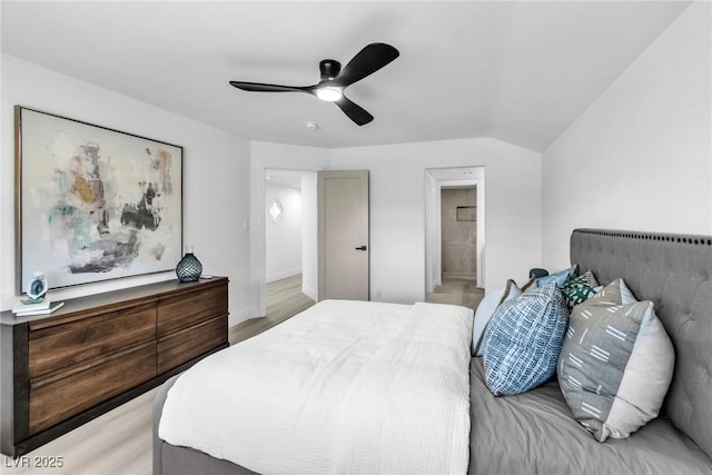 bedroom featuring ceiling fan, light wood finished floors, vaulted ceiling, and ensuite bath