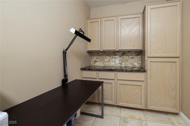 kitchen with dark stone countertops, backsplash, and light brown cabinetry