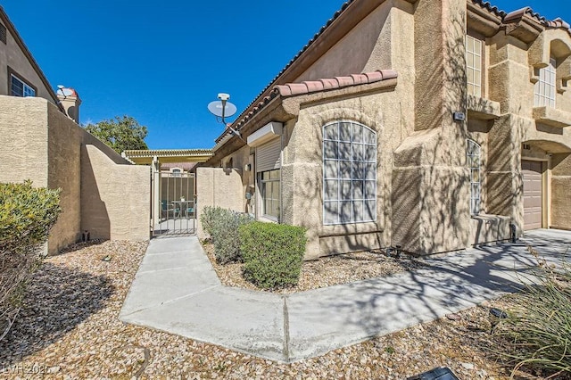 view of side of property with stucco siding, a tile roof, a garage, and a gate