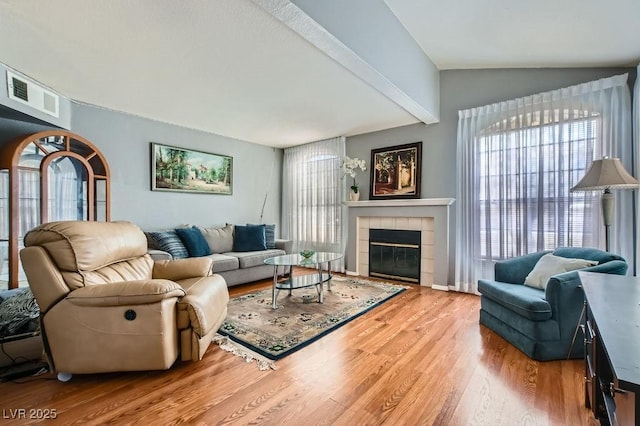 living area featuring visible vents, vaulted ceiling with beams, wood finished floors, and a tiled fireplace