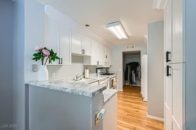 kitchen with white appliances, visible vents, a sink, white cabinets, and light wood-style floors