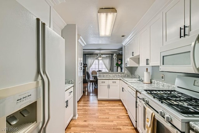 kitchen featuring light wood-style flooring, a sink, white appliances, a peninsula, and white cabinets