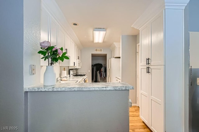 kitchen with white appliances, visible vents, a peninsula, light countertops, and white cabinetry