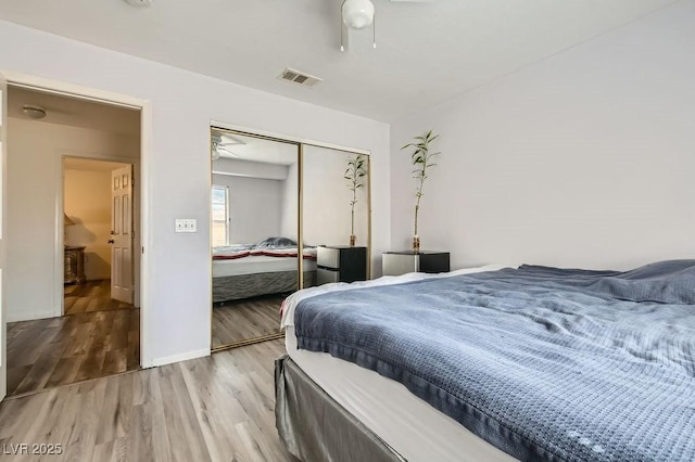 bedroom with a closet, visible vents, baseboards, and wood finished floors