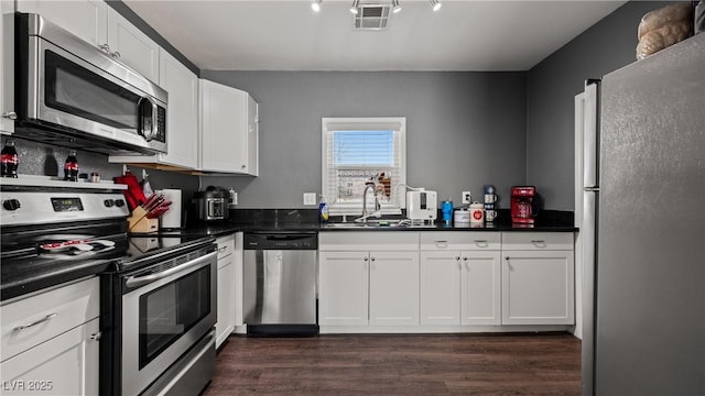 kitchen featuring dark countertops, appliances with stainless steel finishes, a sink, and white cabinets