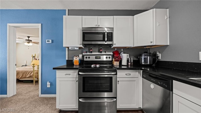 kitchen with white cabinets, stainless steel appliances, carpet floors, and dark countertops