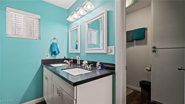 bathroom with wood finished floors, baseboards, a sink, and double vanity