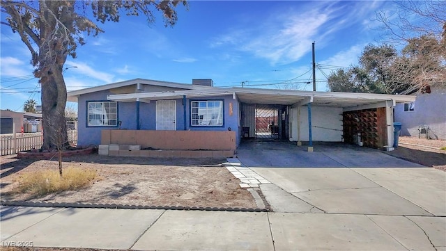 view of front of home with an attached carport, concrete driveway, fence, and stucco siding