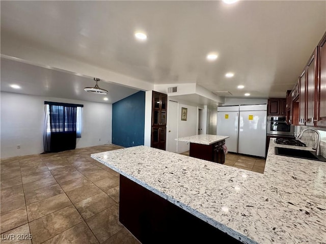 kitchen featuring recessed lighting, a sink, a center island, white refrigerator, and light stone countertops