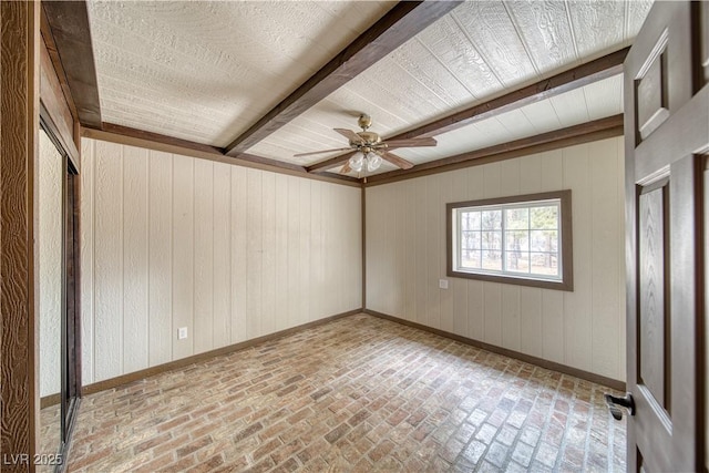 empty room with brick floor, beamed ceiling, baseboards, and ceiling fan