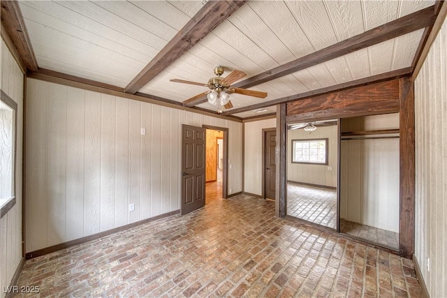 unfurnished bedroom with a ceiling fan, brick floor, beam ceiling, wood walls, and a closet