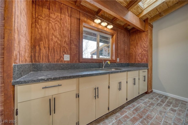 kitchen with brick floor, a sink, wooden walls, and baseboards