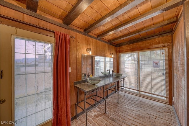 dining room featuring brick floor, beamed ceiling, wooden ceiling, and wooden walls