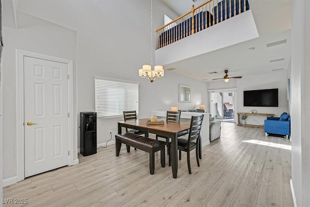 dining space featuring ceiling fan with notable chandelier, a high ceiling, light wood-type flooring, and baseboards