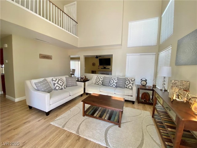 living area featuring visible vents, a high ceiling, light wood-style flooring, and baseboards