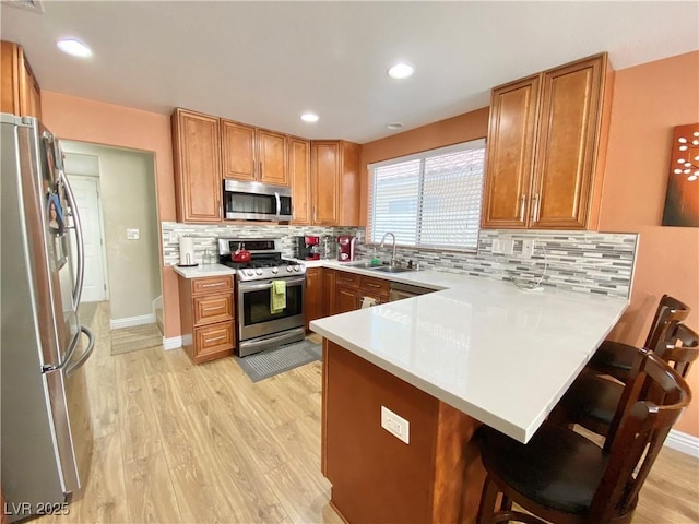 kitchen with a peninsula, stainless steel appliances, light countertops, a kitchen bar, and a sink