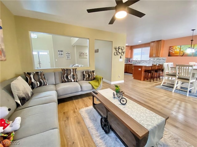 living room with light wood-style floors, ceiling fan, and baseboards