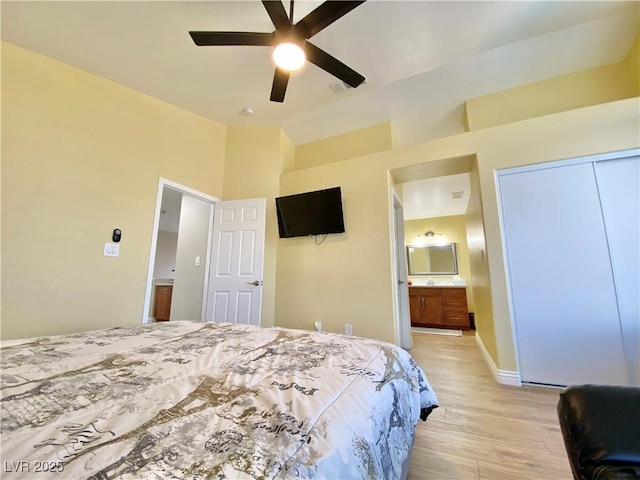 bedroom with light wood-style floors, vaulted ceiling, ceiling fan, ensuite bath, and baseboards