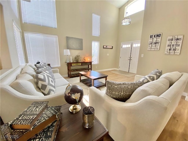 living room featuring light wood finished floors, a towering ceiling, and baseboards