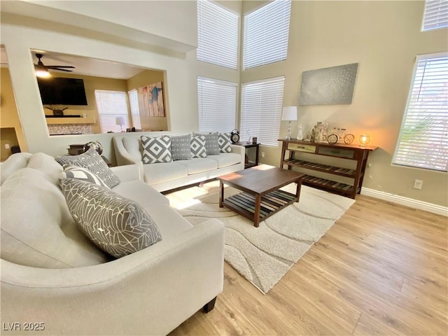 living area with ceiling fan, a towering ceiling, baseboards, and wood finished floors