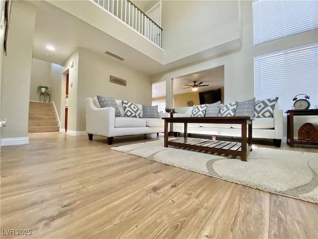 living room featuring baseboards, visible vents, a high ceiling, stairs, and light wood-style floors