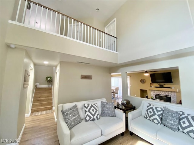 living room with visible vents, a tiled fireplace, a towering ceiling, wood finished floors, and stairs