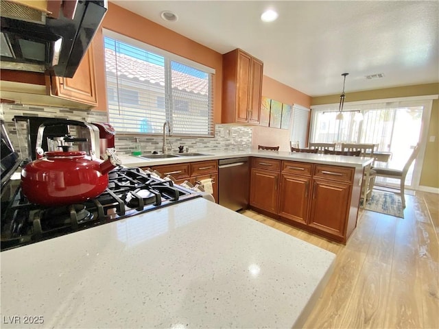 kitchen featuring a sink, light countertops, stainless steel dishwasher, brown cabinets, and pendant lighting