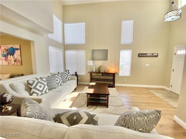 living room with light wood-style flooring, a towering ceiling, and baseboards