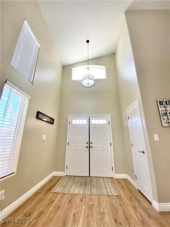 foyer entrance with baseboards, a high ceiling, and light wood-style floors