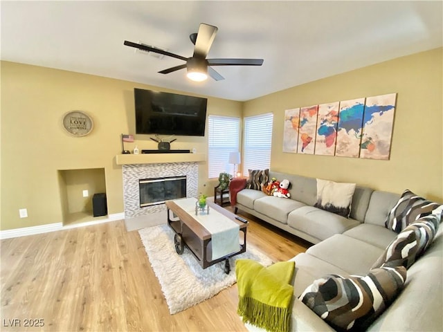 living room featuring light wood finished floors, a tile fireplace, a ceiling fan, and baseboards