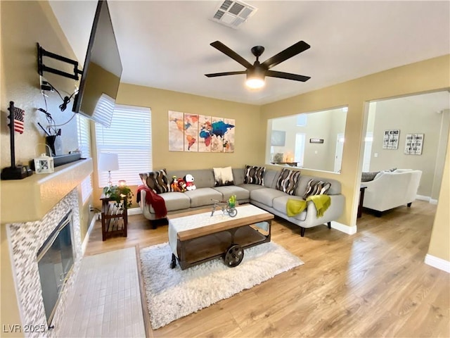 living room with visible vents, light wood-style floors, ceiling fan, a tile fireplace, and baseboards