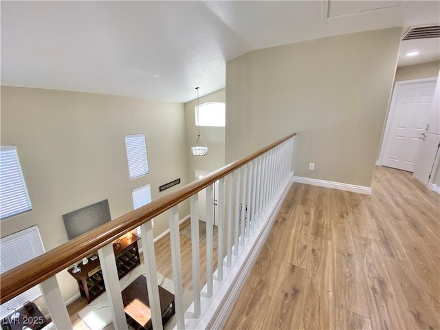 corridor with lofted ceiling, visible vents, light wood-style floors, an upstairs landing, and baseboards