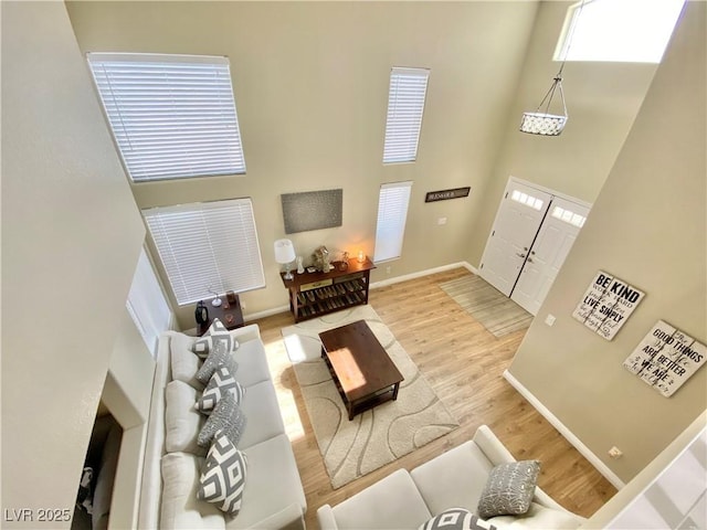 living room featuring a towering ceiling, light wood finished floors, and baseboards