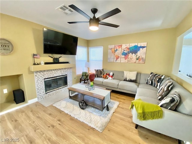 living room featuring visible vents, light wood-style flooring, a ceiling fan, a tile fireplace, and baseboards