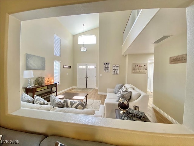 living area featuring visible vents, a towering ceiling, baseboards, and wood finished floors