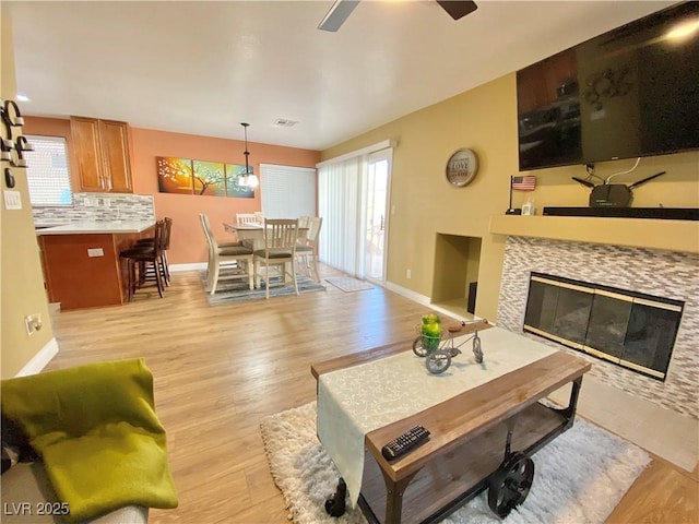 living room with light wood-style floors, visible vents, a tiled fireplace, and baseboards