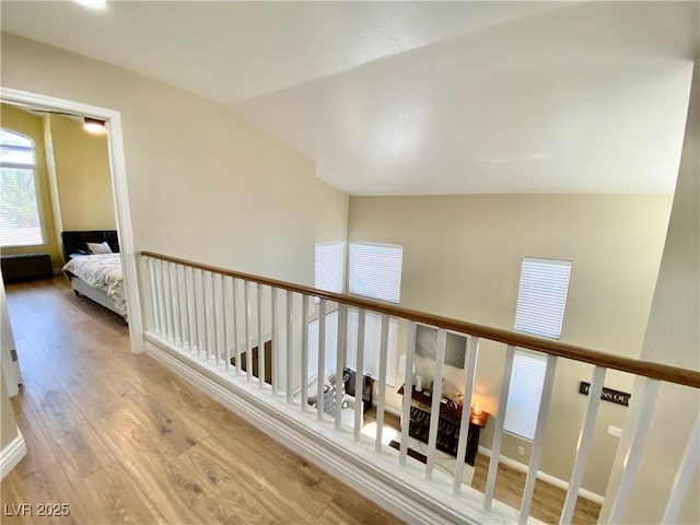 hall featuring light wood-type flooring, baseboards, and vaulted ceiling