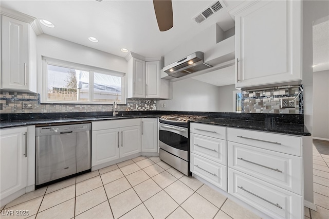 kitchen featuring visible vents, dark stone counters, stainless steel appliances, white cabinetry, and a sink