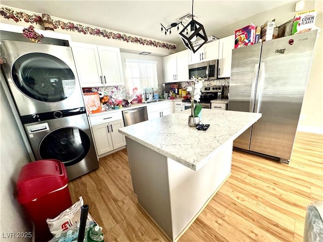 kitchen with white cabinets, stacked washer / dryer, appliances with stainless steel finishes, a center island, and pendant lighting