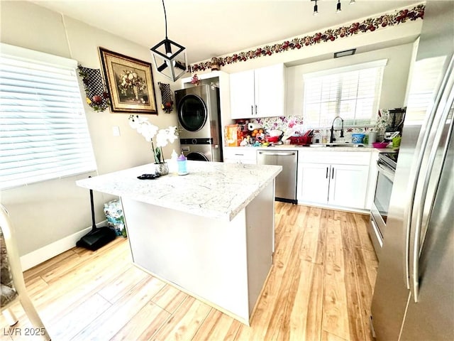 kitchen with stainless steel appliances, a kitchen island, white cabinets, stacked washer / drying machine, and hanging light fixtures