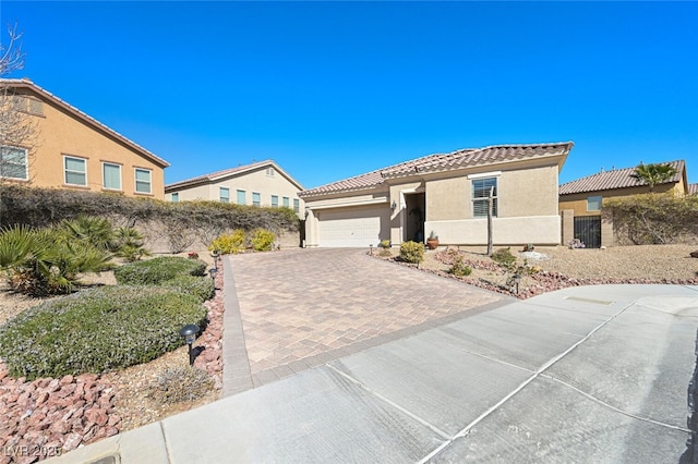 mediterranean / spanish-style home with decorative driveway, stucco siding, fence, a garage, and a tiled roof