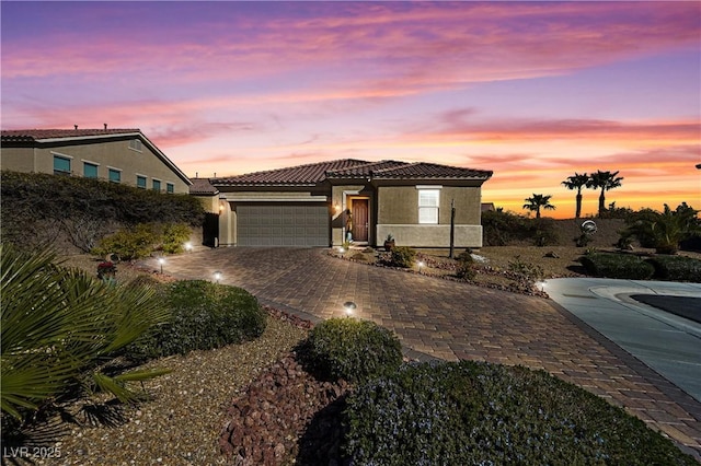 mediterranean / spanish-style home with a garage, decorative driveway, a tiled roof, and stucco siding