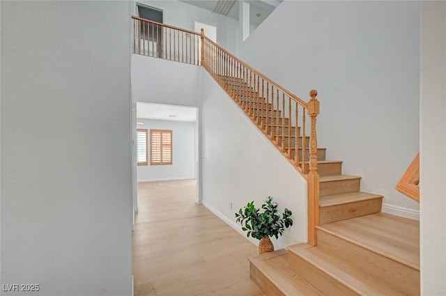 stairs with a high ceiling, baseboards, and wood finished floors