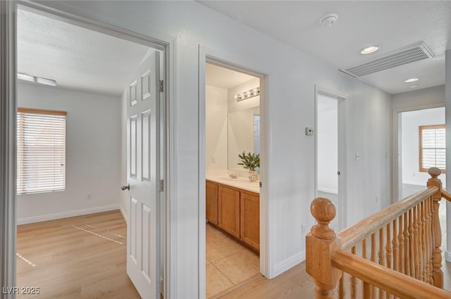 corridor featuring baseboards, visible vents, light wood finished floors, and an upstairs landing