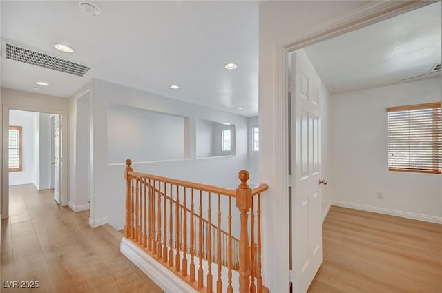 hall with light wood-style flooring, visible vents, a wealth of natural light, and an upstairs landing