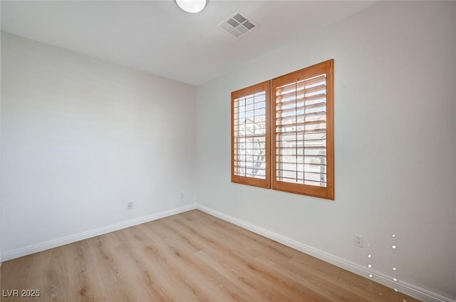 spare room featuring wood finished floors, visible vents, and baseboards