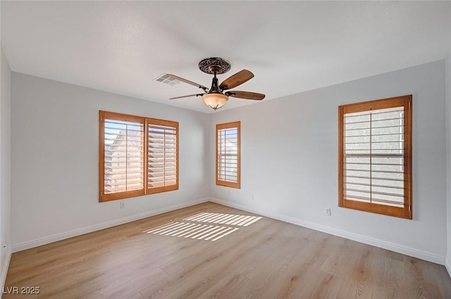 spare room with light wood-type flooring, visible vents, ceiling fan, and baseboards