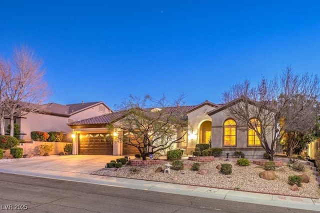 mediterranean / spanish house featuring an attached garage, a tile roof, concrete driveway, and stucco siding