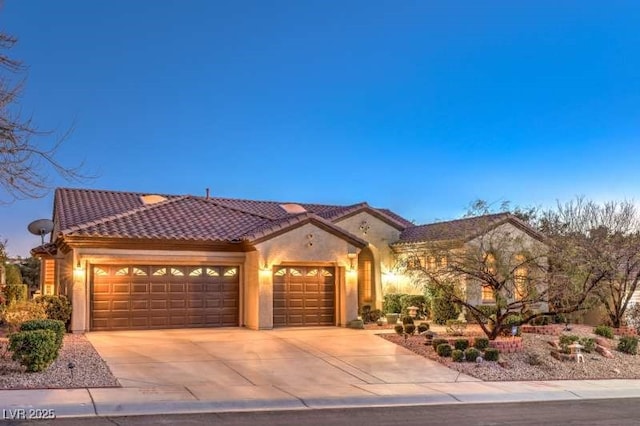 mediterranean / spanish-style home featuring concrete driveway, an attached garage, a tiled roof, and stucco siding